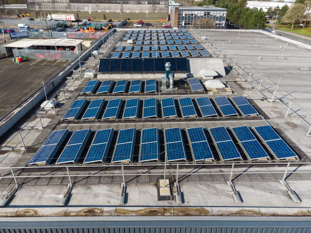 Aerial view of a flat rooftop covered with multiple rows of solar panels under clear daylight.