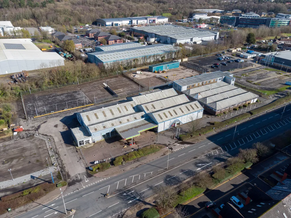 Aerial view of an industrial complex with multiple warehouse buildings, parking lots, and surrounding roads in a semi-urban area.