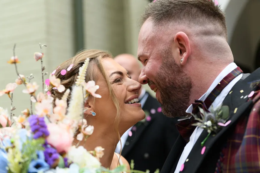 Close-up of a smiling bride and groom touching noses with confetti falling around them.