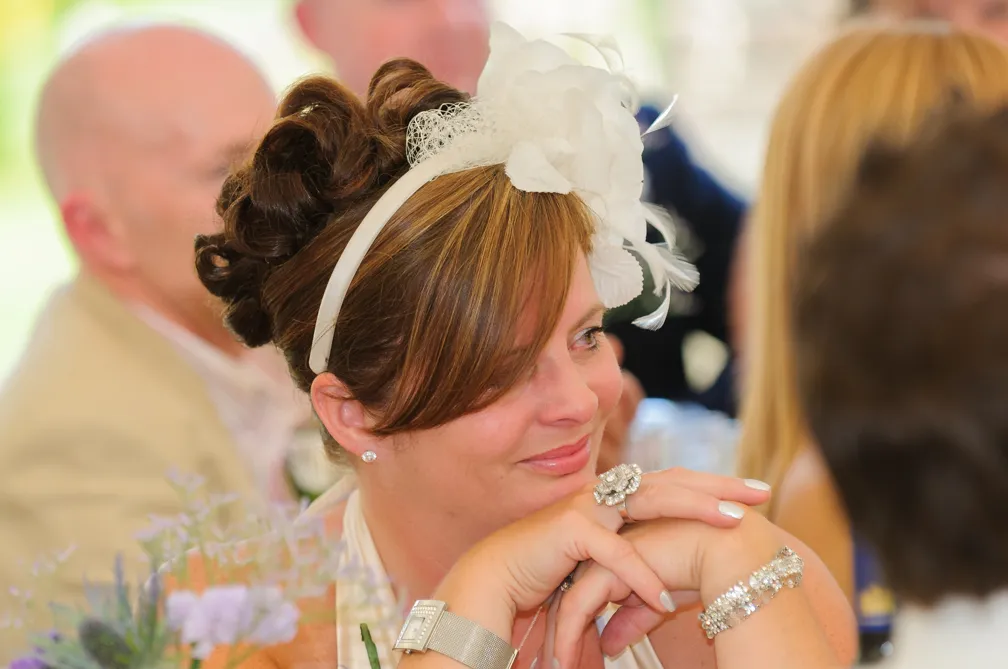 Woman with curled hair wearing a white floral headband, silver jewelry, and resting her chin on her hands at a social event.