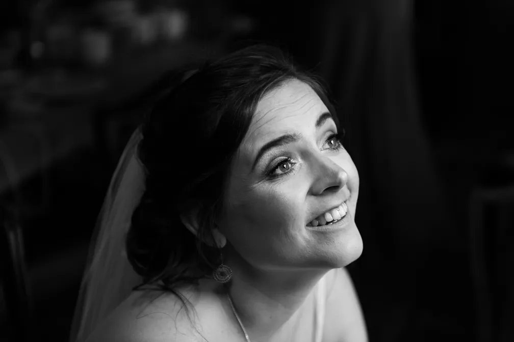 Smiling bride with veil looking upwards in a black and white portrait.