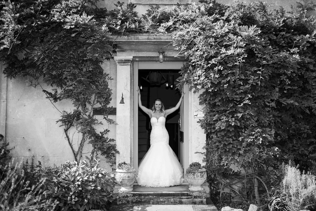 Bride in a strapless mermaid wedding gown standing in a stone doorway surrounded by lush greenery and climbing plants.