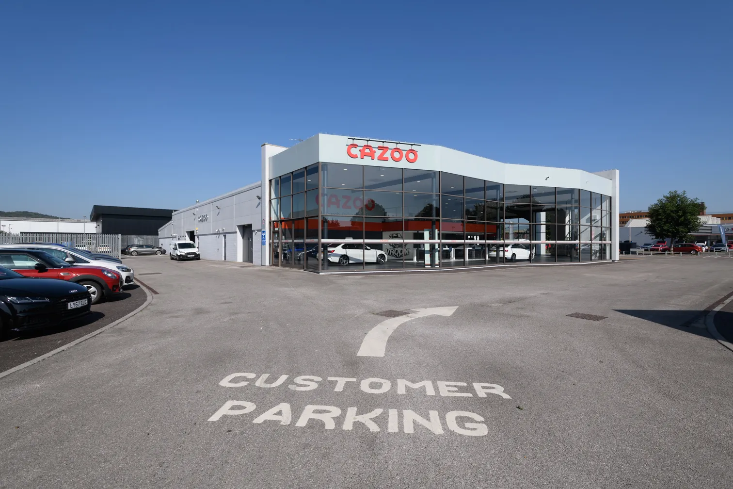 Modern Cazoo car dealership building with large glass windows and customer parking area in front.