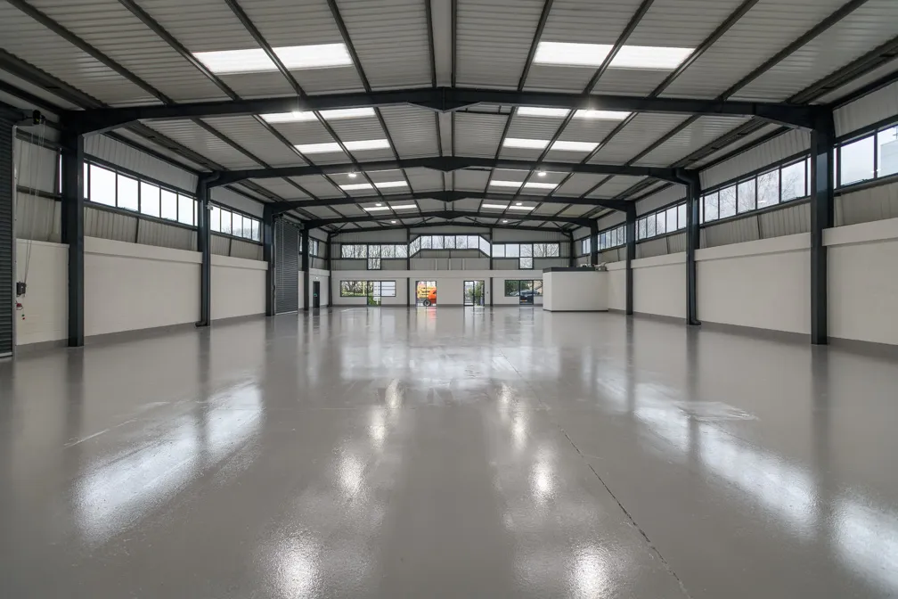 Empty large industrial warehouse with polished concrete floor, steel beams, and multiple windows.