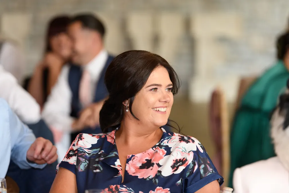 Smiling woman with dark hair wearing a navy blue floral dress at an indoor event.