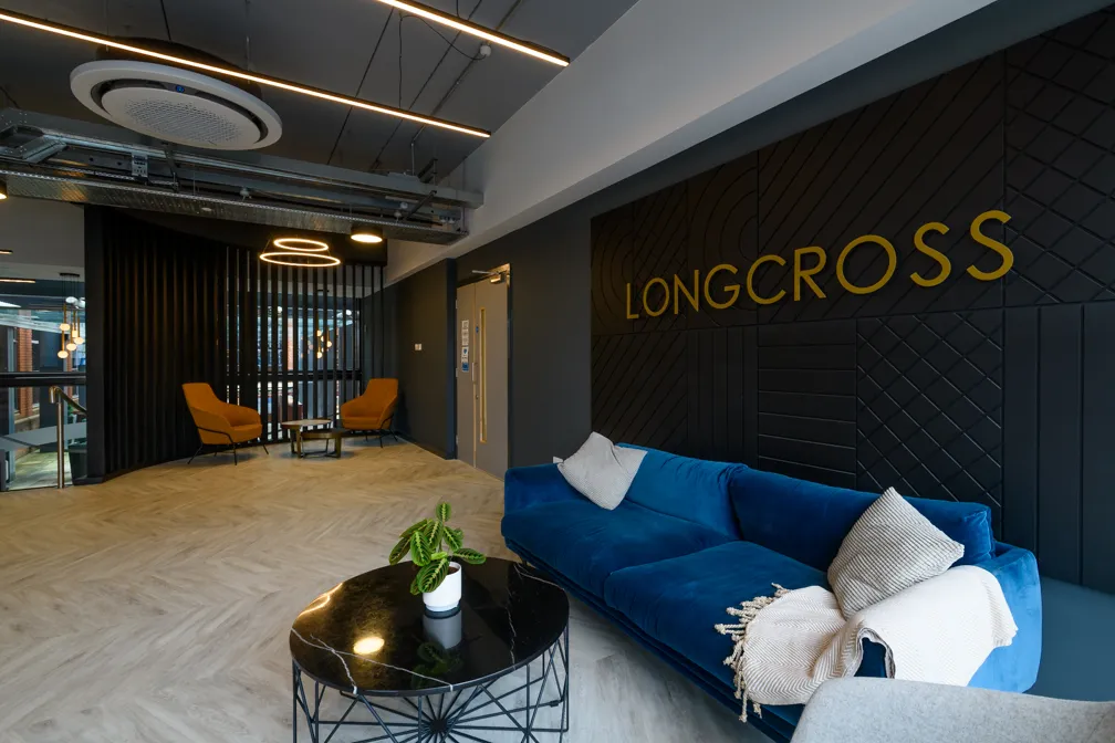 Modern office lounge with a blue velvet sofa, two mustard chairs, a black marble coffee table, and a wall sign reading LONGCROSS.