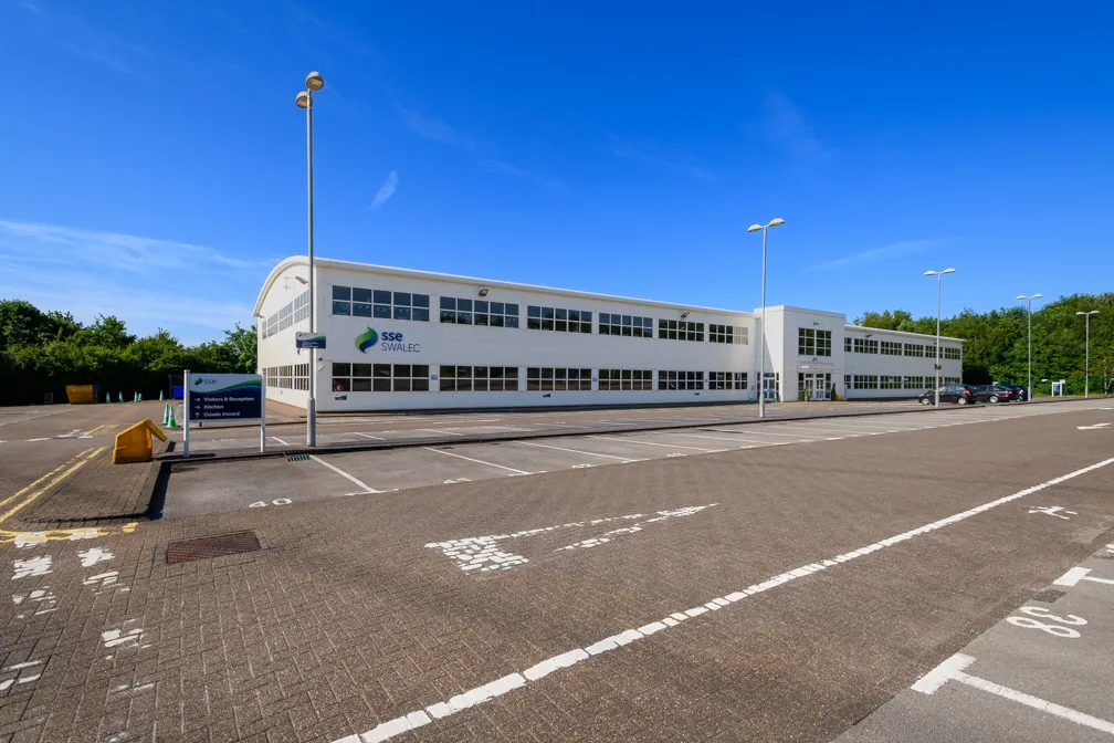Wide view of a two-story white office building with SSE SWALEC signage, surrounded by an empty parking lot under a clear blue sky.
