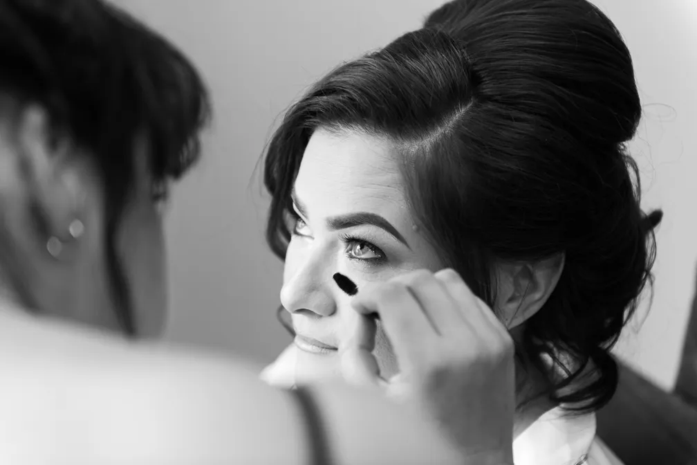 Woman with styled hair looking upward as another person applies makeup under her eye with a brush.