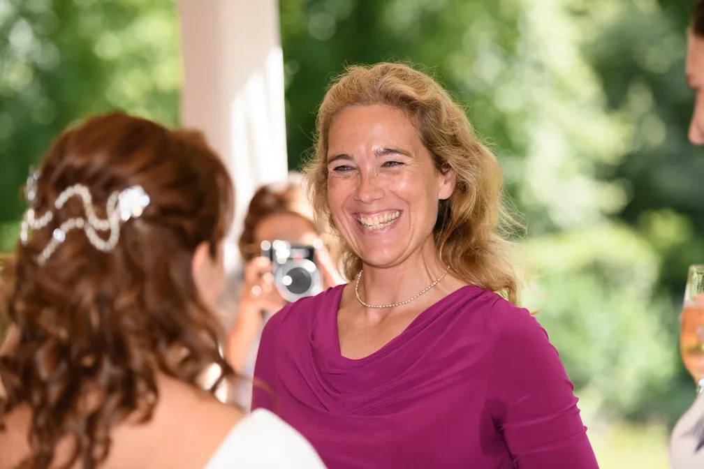 Smiling woman in a purple dress with blonde hair talking to another person with decorated brown hair at an outdoor event.