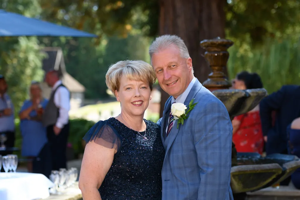 Couple dressed formally posing outdoors near a stone fountain at a social event.