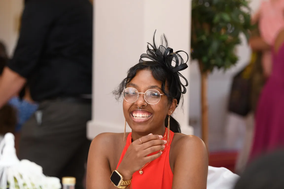 Smiling woman wearing glasses, a black decorative headpiece, and a red dress at an indoor event.