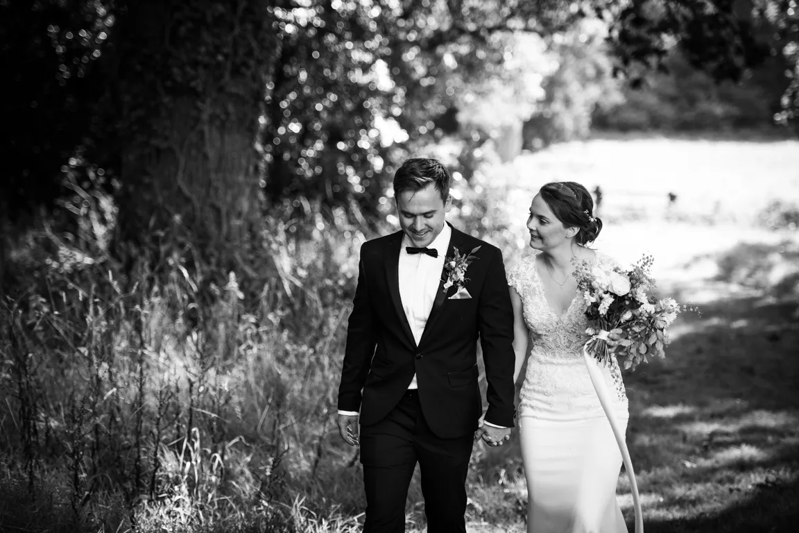 Bride and groom holding hands and walking outdoors, the bride holding a bouquet of flowers.