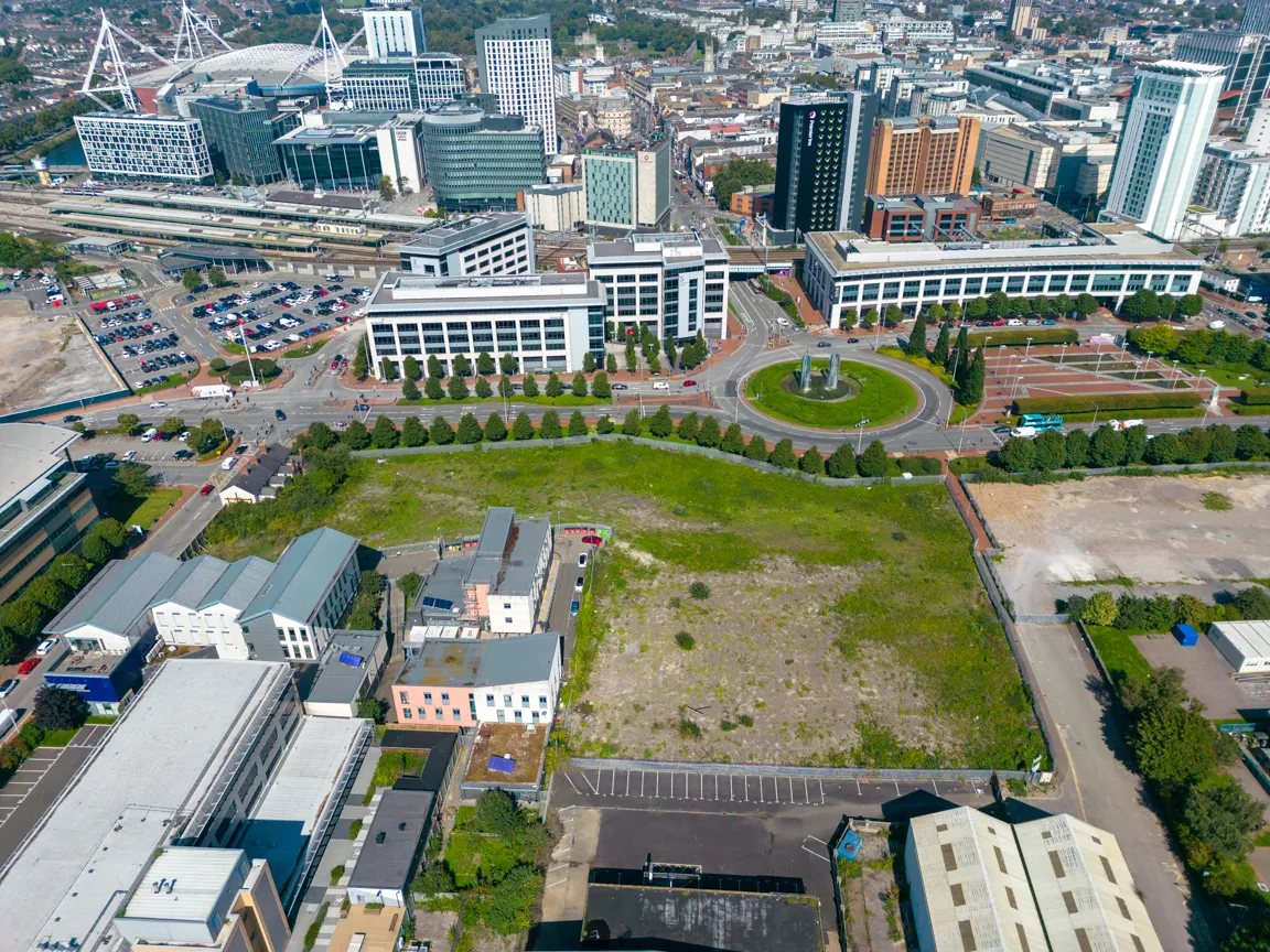 Aerial view of an urban area featuring office buildings, a roundabout with a fountain, parking lots, and a large vacant grassy lot.