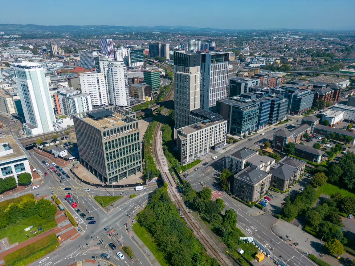 Aerial view of an urban area with modern high-rise buildings, railway tracks running through the center, and busy streets with vehicles and pedestrians.