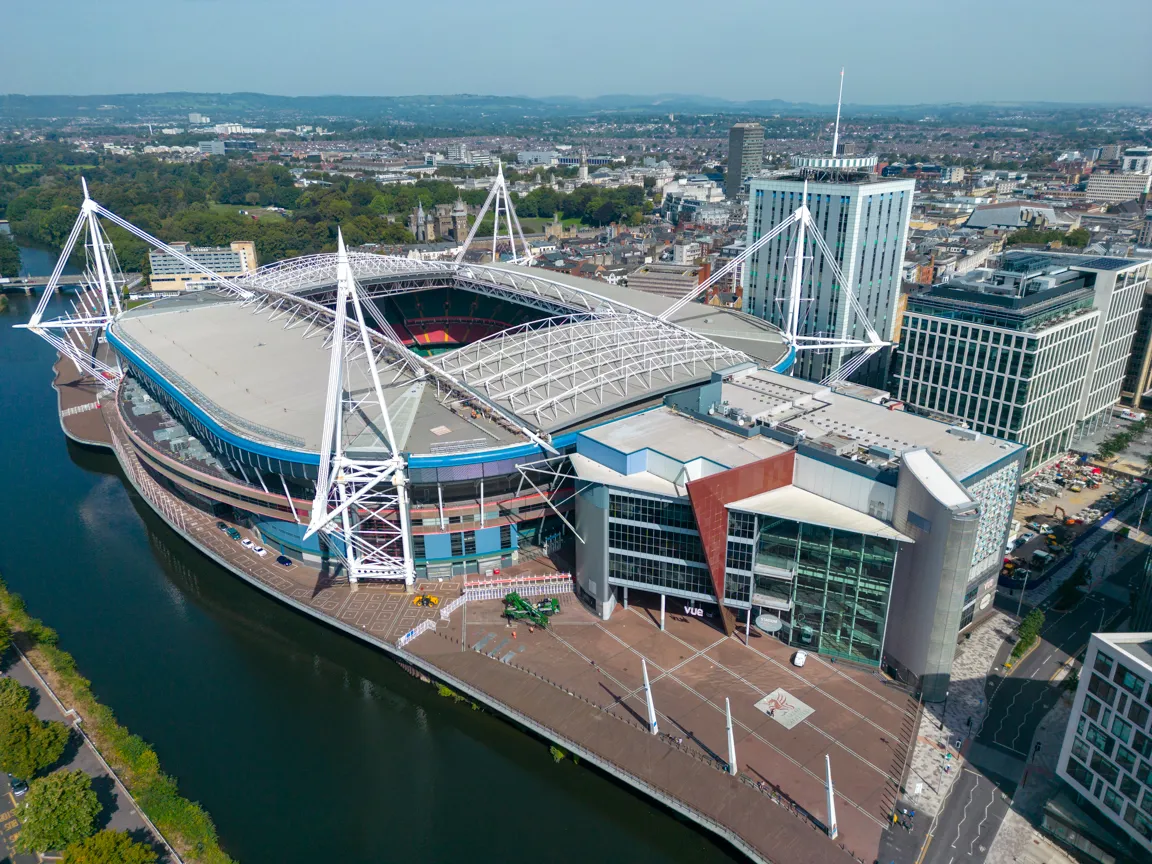 Aerial view of a large modern stadium by a river with surrounding city buildings and green spaces.