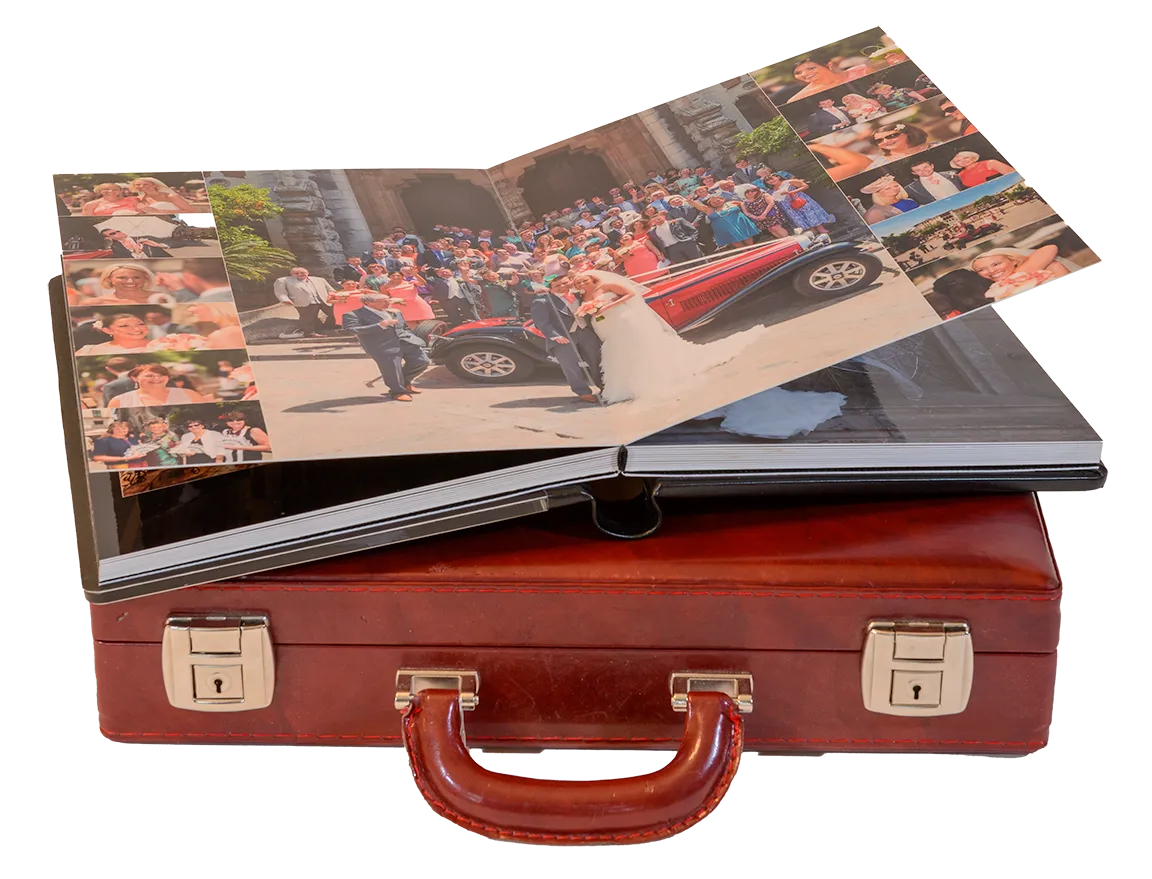 Open wedding photo album on top of a closed brown leather briefcase, showing a bride and groom with guests around a red vintage car.
