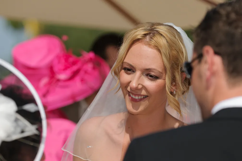 Smiling bride with blonde hair and veil looking at a man in a suit.