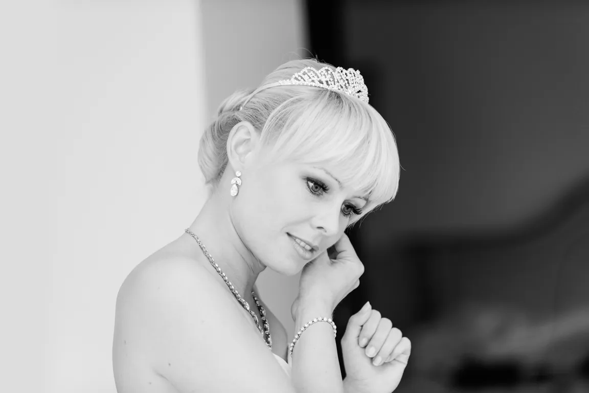 Bride with short blonde hair wearing a tiara, earrings, necklace, and bracelet, adjusting an earring.