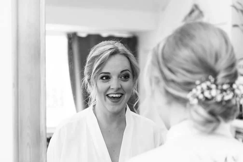 Smiling woman with hair up decorated with flowers looking at her reflection in a mirror.