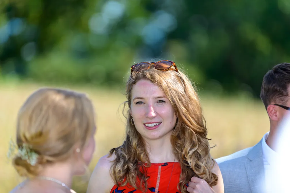 Young woman with curly blonde hair wearing a red dress and sunglasses on her head, smiling outdoors.