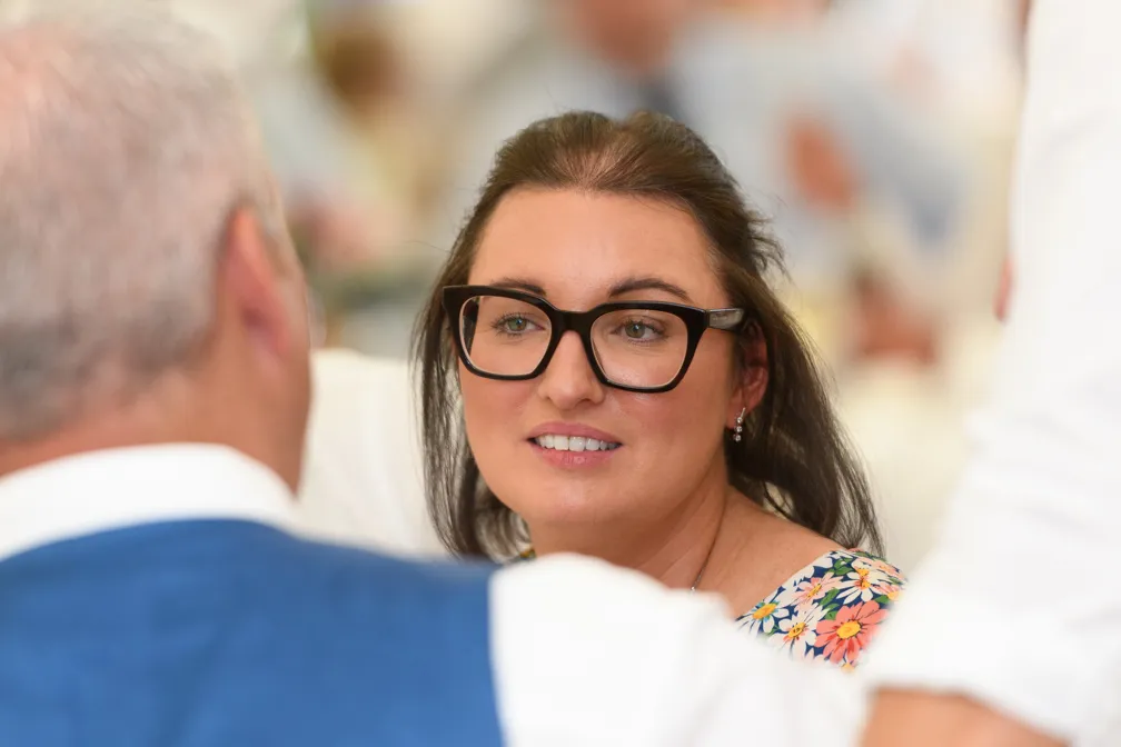 Woman with glasses and floral dress smiling and engaging in conversation with a man in a blue suit.