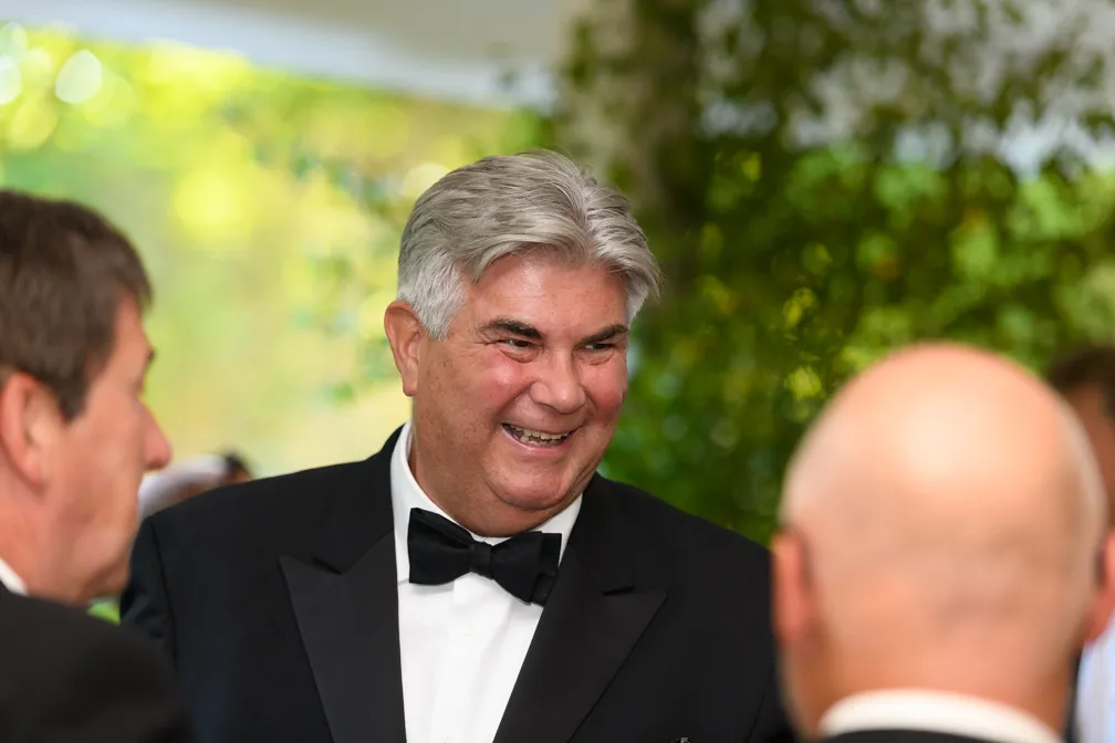 Smiling older man with gray hair wearing a black tuxedo and bow tie at a social event.