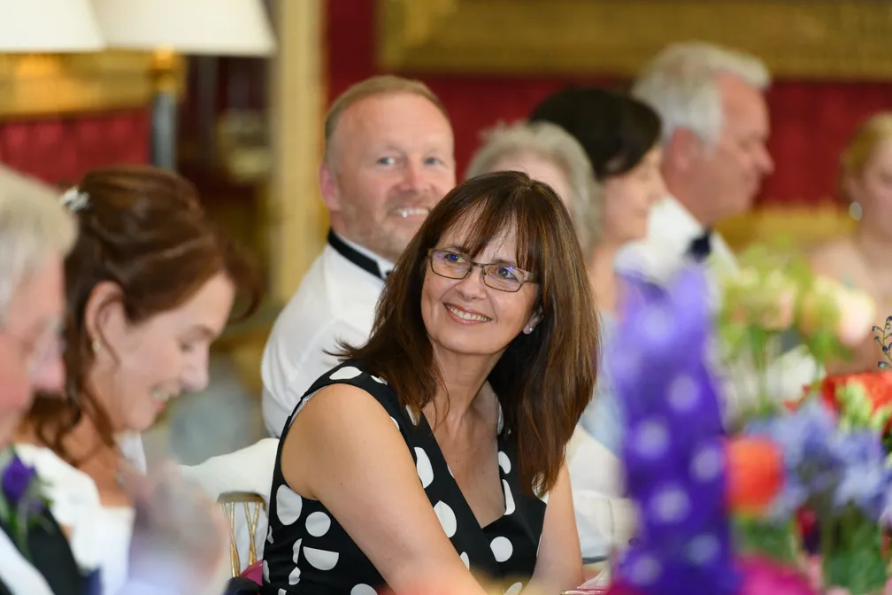Smiling woman in black dress with white polka dots sitting at a formal event table with other guests.