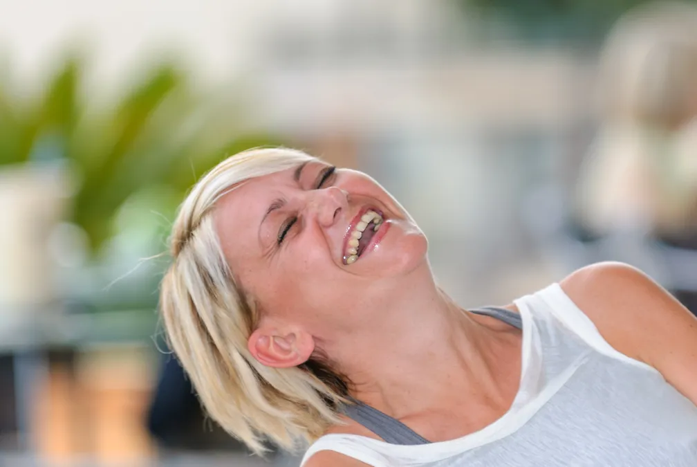 Middle-aged woman with short blonde hair laughing joyfully with eyes closed.