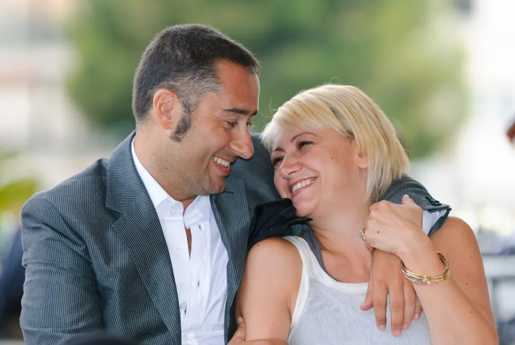 Smiling man in a gray suit embraces and looks affectionately at a smiling woman in a white tank top.