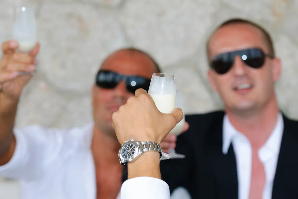 Two men in sunglasses raising glasses filled with a white drink in a toast.