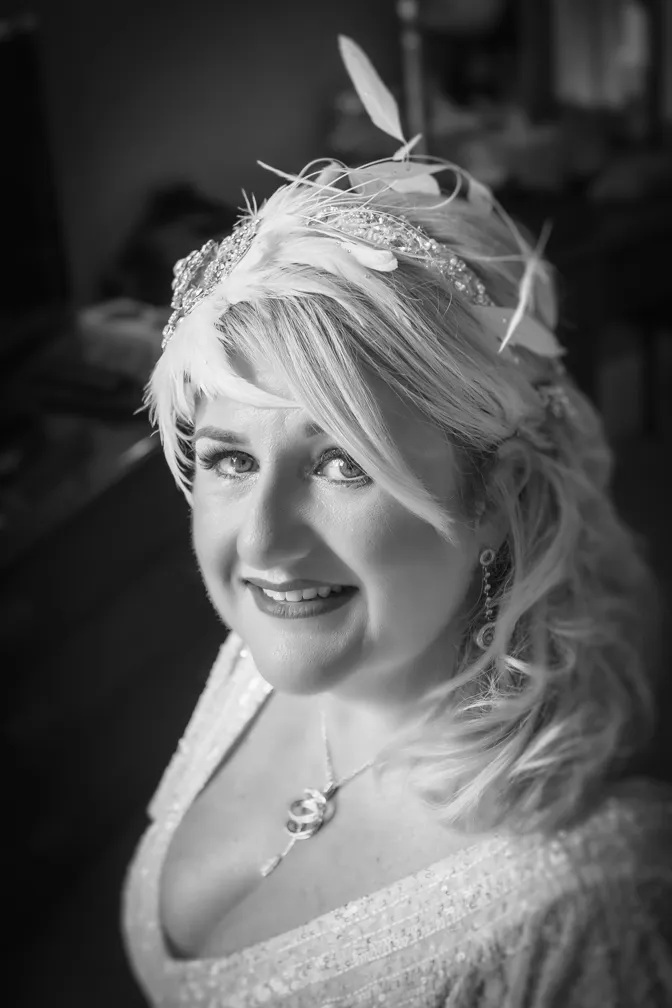 Smiling woman with light hair wearing a decorative feathered headpiece and a necklace.