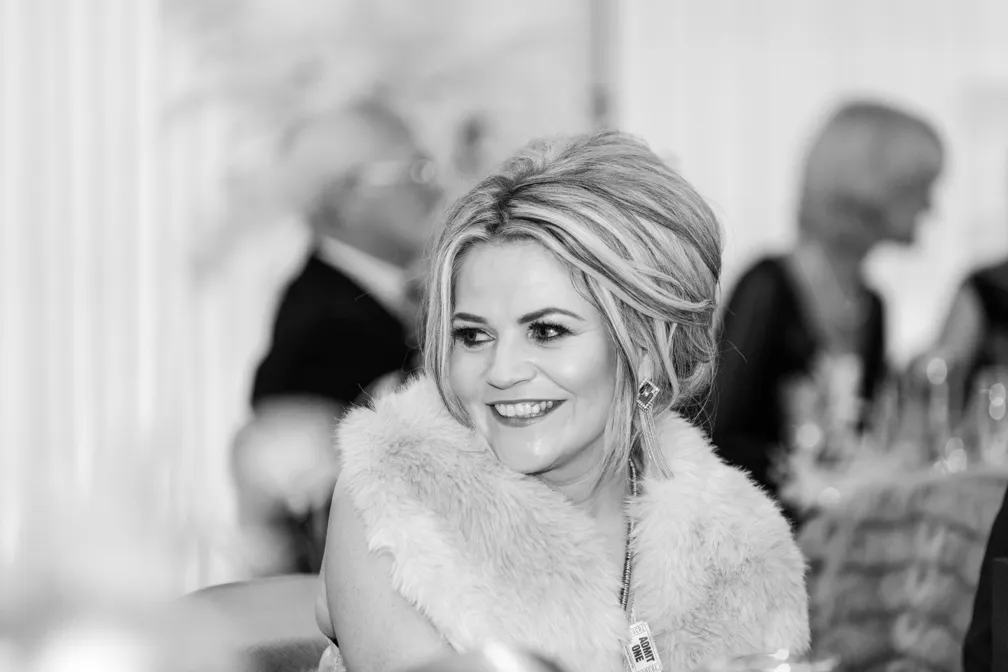 Smiling woman with styled hair wearing a fur stole and earrings at a formal event.
