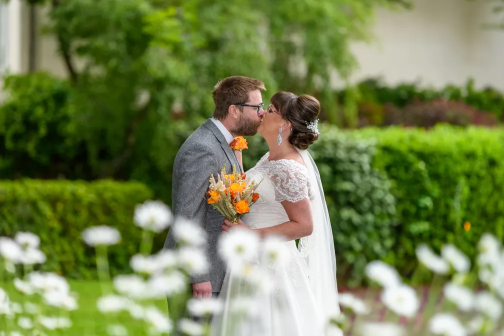 Bride & groom kissing with daisies in foreground in gardens at Glen yr Afon hotel Usk