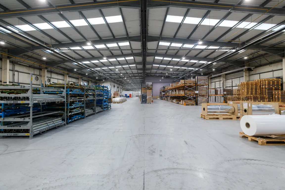 Spacious industrial warehouse with metal pipes and pallets stored on racks and the floor.