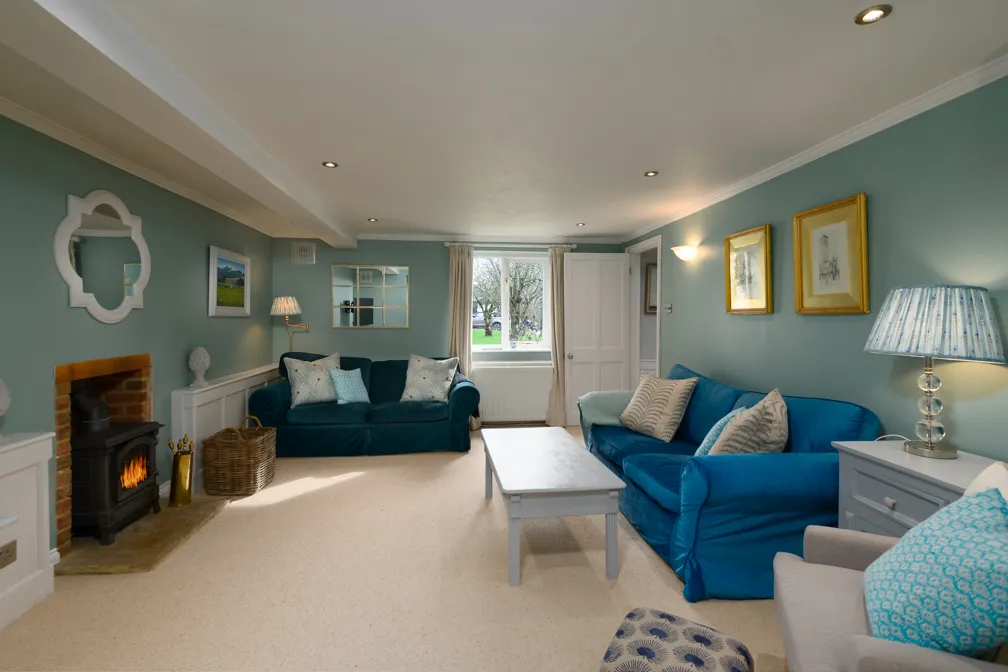 Cozy living room with blue sofas, beige carpet, a white coffee table, a lit fireplace, and light blue walls with framed art and decorative mirrors.