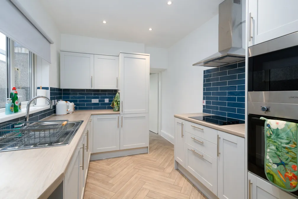 Modern kitchen with white cabinets, blue subway tile backsplash, wood-patterned herringbone floor, and stainless steel appliances.