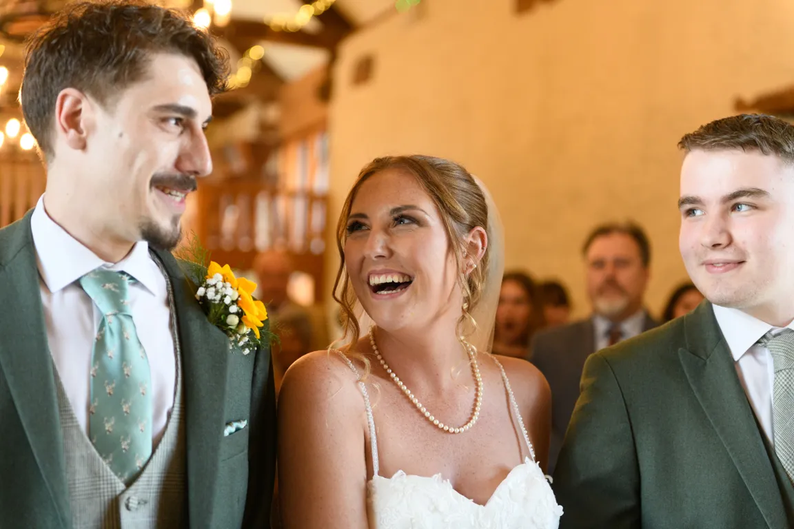Bride smiling between two men in suits during a wedding ceremony.