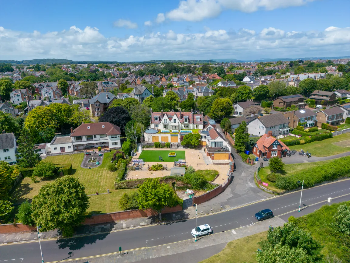 Aerial view of a residential neighborhood with various houses surrounded by green trees and lawns under a partly cloudy sky.