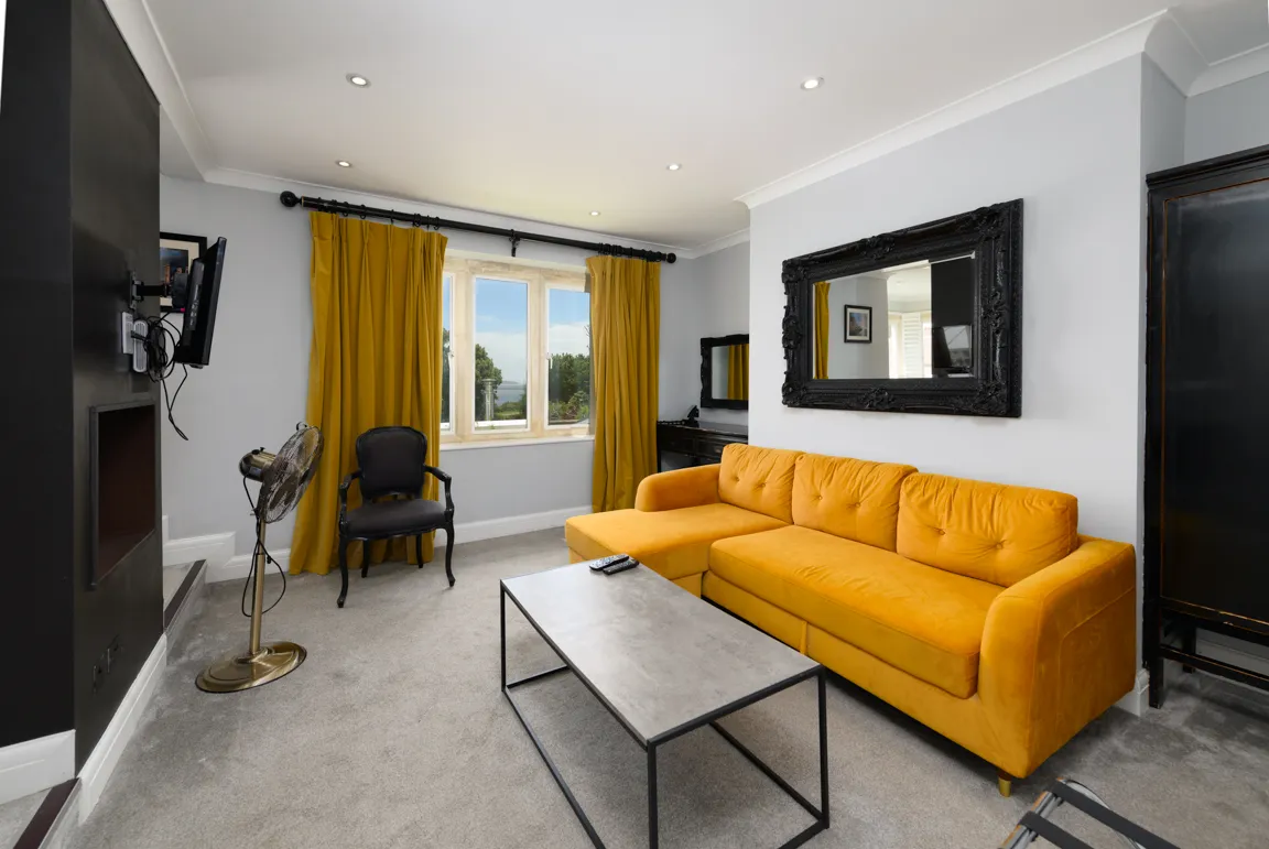 Modern living room with mustard yellow sectional sofa, gray carpet, black armchair, rectangular coffee table, and large window with mustard curtains.