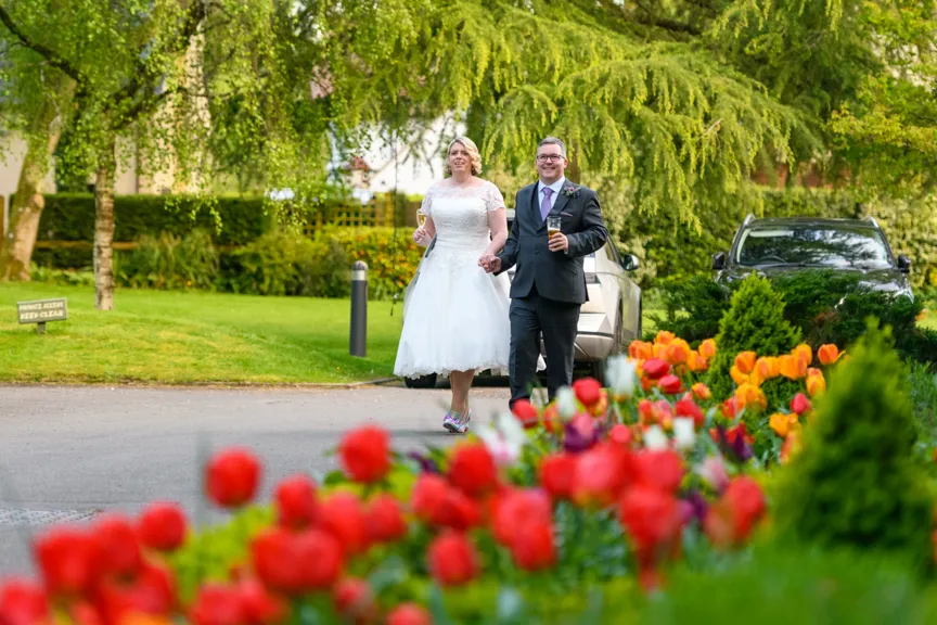Bride and groom walking hand in hand on a path near colorful tulip flowers and greenery.