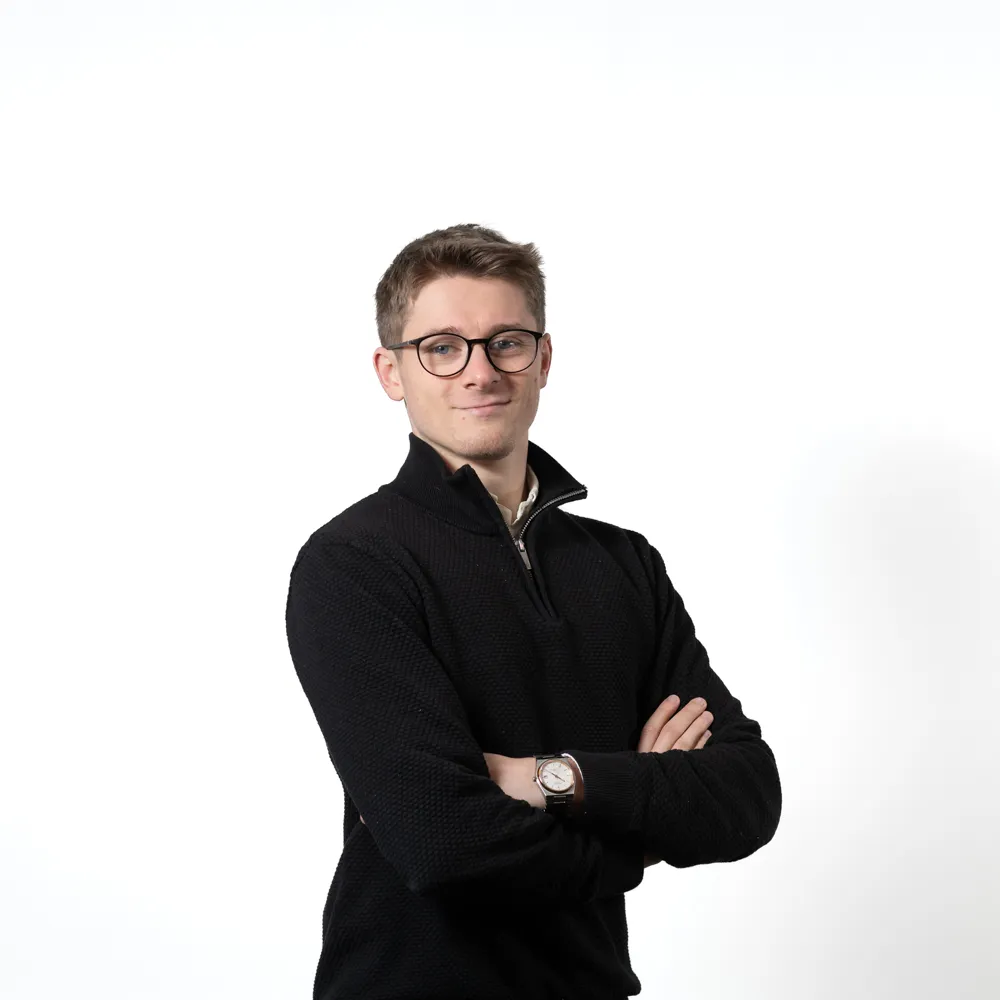 Young man with glasses wearing a black sweater and crossed arms against a white background.