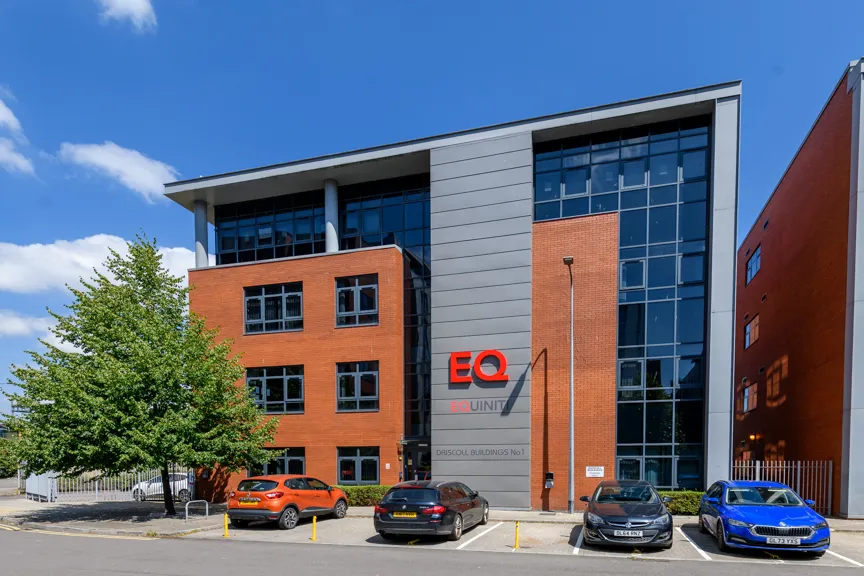 Modern office building with red brick and glass facade displaying 'EQ EQUINITI' and parking lot with several cars under a blue sky.