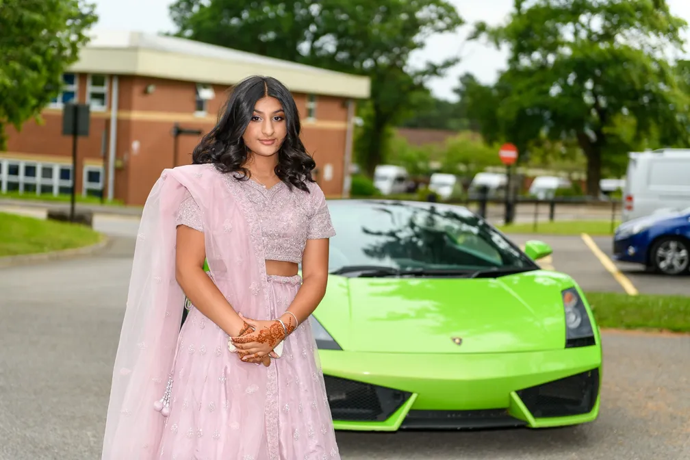 Young woman in a pink traditional outfit with henna on her hands standing in front of a green Lamborghini sports car.