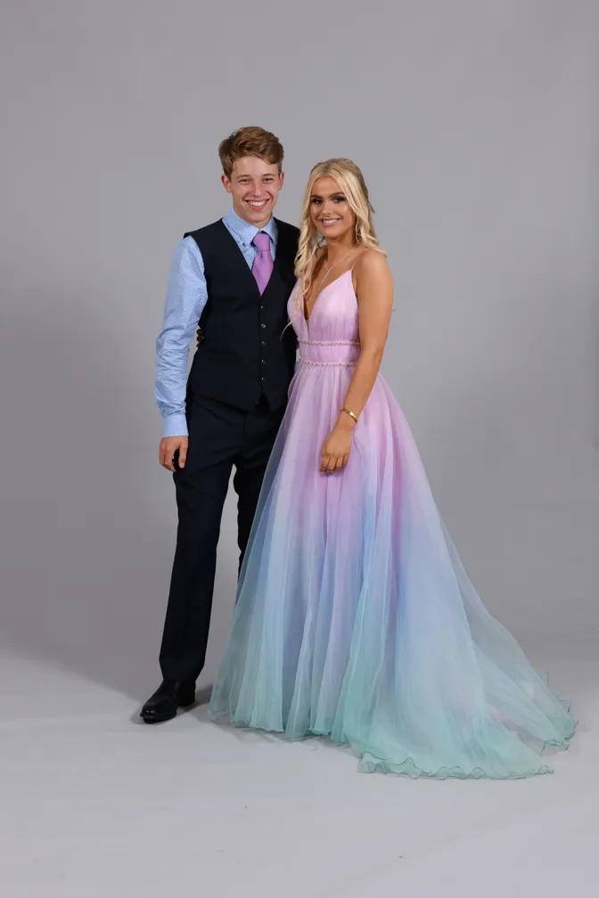 Young couple posing together, the man in a black vest suit with a purple tie and the woman in a pastel ombre gown with shades of pink, purple, and blue.