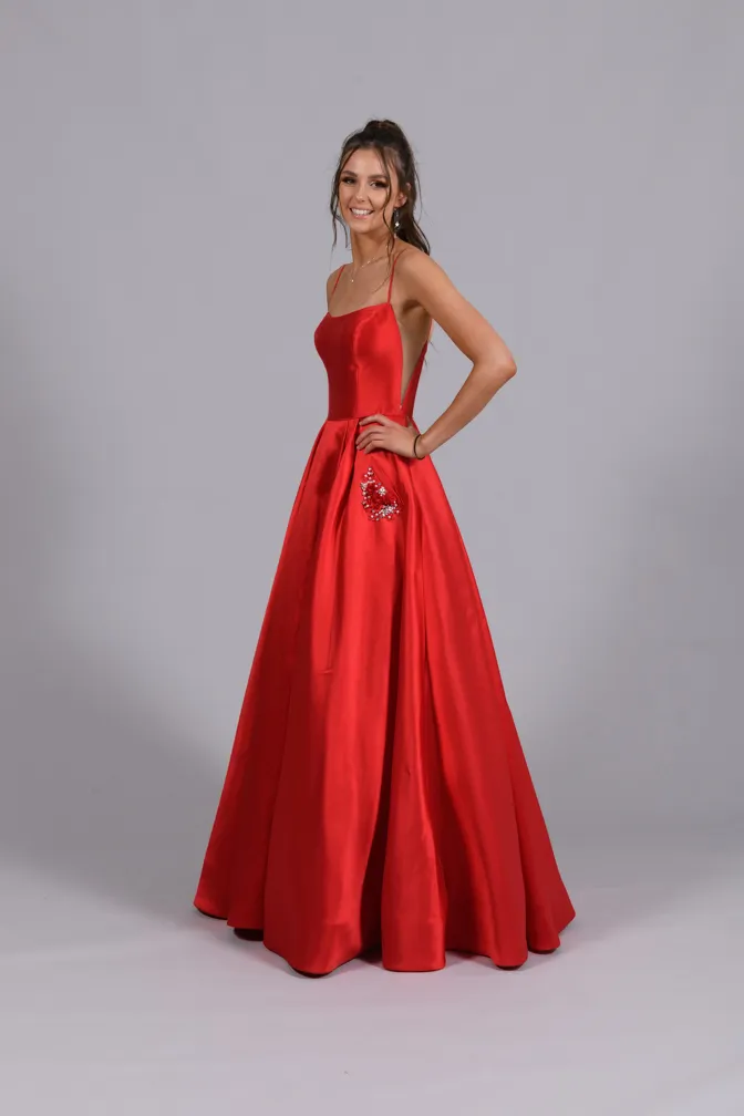 Smiling woman posing in a floor-length red satin gown with thin straps and floral embellishment on the skirt.