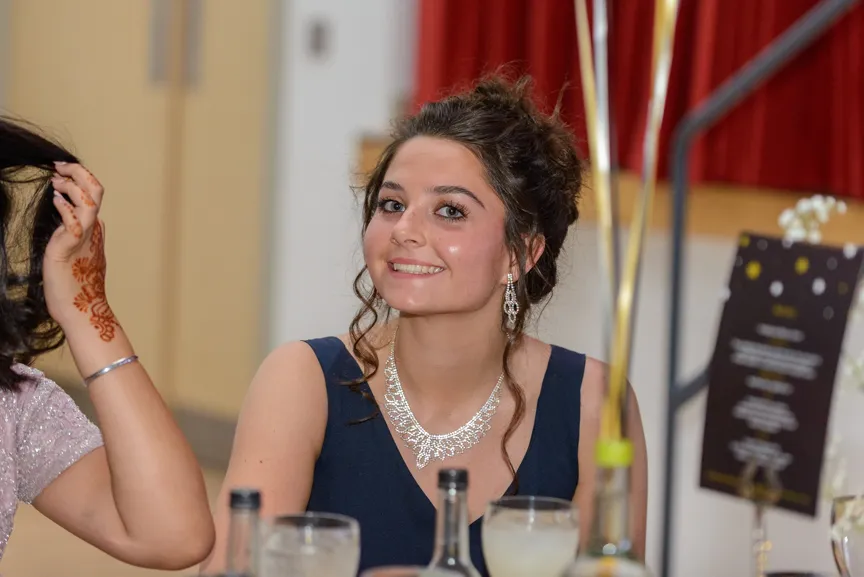Young woman with curled hair wearing a navy dress and silver jewelry smiling at a formal event.