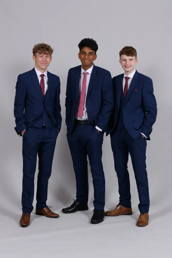 Three young men wearing navy blue suits, white shirts, and red ties standing against a plain gray background.