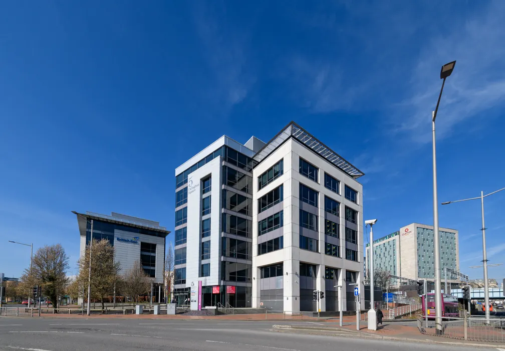 Modern office buildings along a street with a clear blue sky and sparse pedestrian presence.