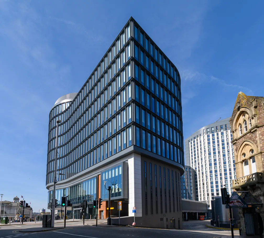 Modern glass and steel office building with rounded edges under a clear blue sky in an urban area.