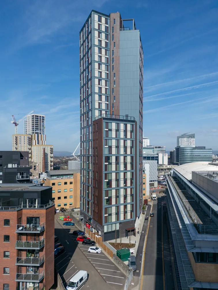 Tall modern residential and commercial high-rise building in an urban area with clear blue sky and surrounding smaller buildings.